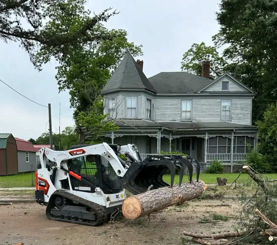 Crane with grapple removing pine leaning over roof