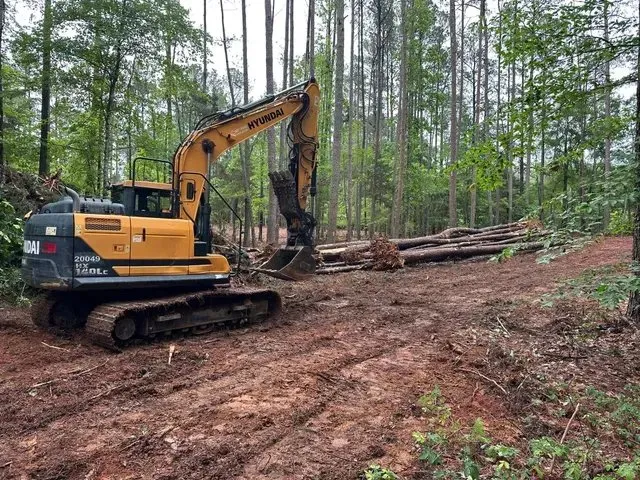 Hyundai excavator digging into red clay on a land clearing project