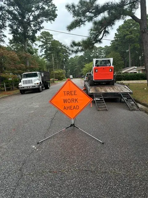 Tree work ahead sign next to chipper at a storm cleanup site